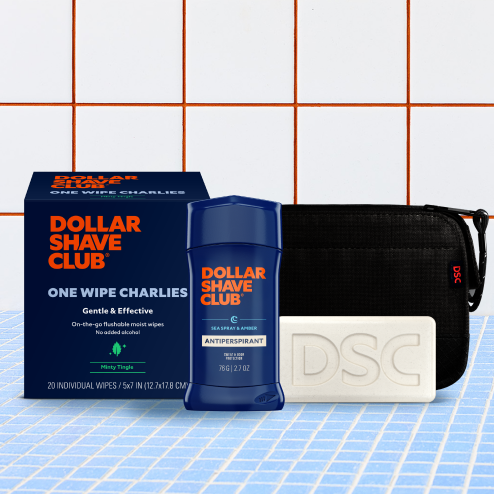 Dollar Shave Club products including wipes, antiperspirant, and soap on a tiled bathroom floor.
