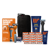 Dollar Shave Club University of Texas grooming kit on a white background. Includes a burnt orange razor handle with the Texas Longhorns logo, 24 blades, Shave Butter, Prep Scrub, a black 3-in-1 electric trimmer, and a black traveler case.